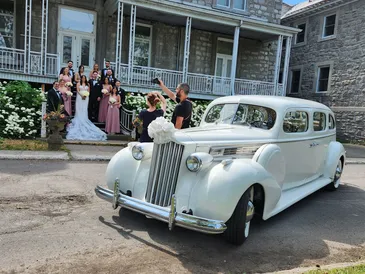 Vintage white wedding car with wedding party nearby